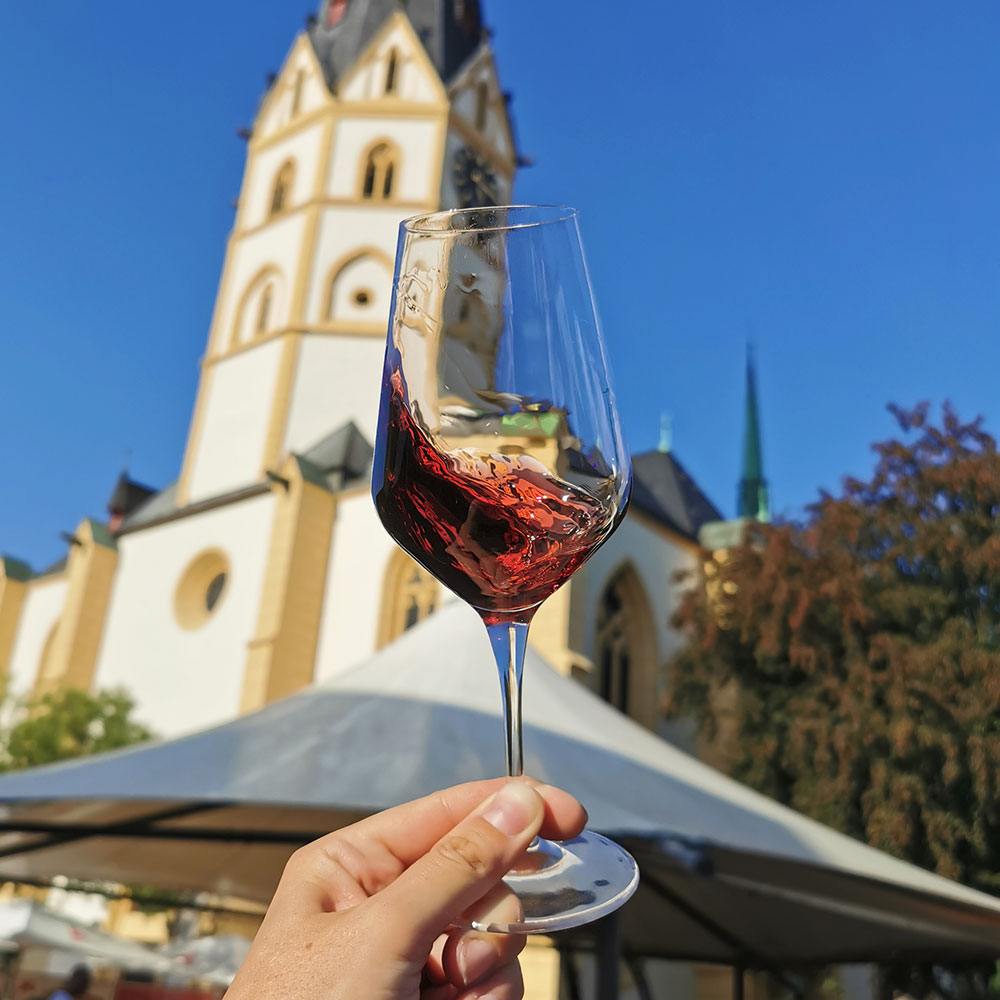 geschwenktes Rotweinglas vor der Kirche St. Laurentius